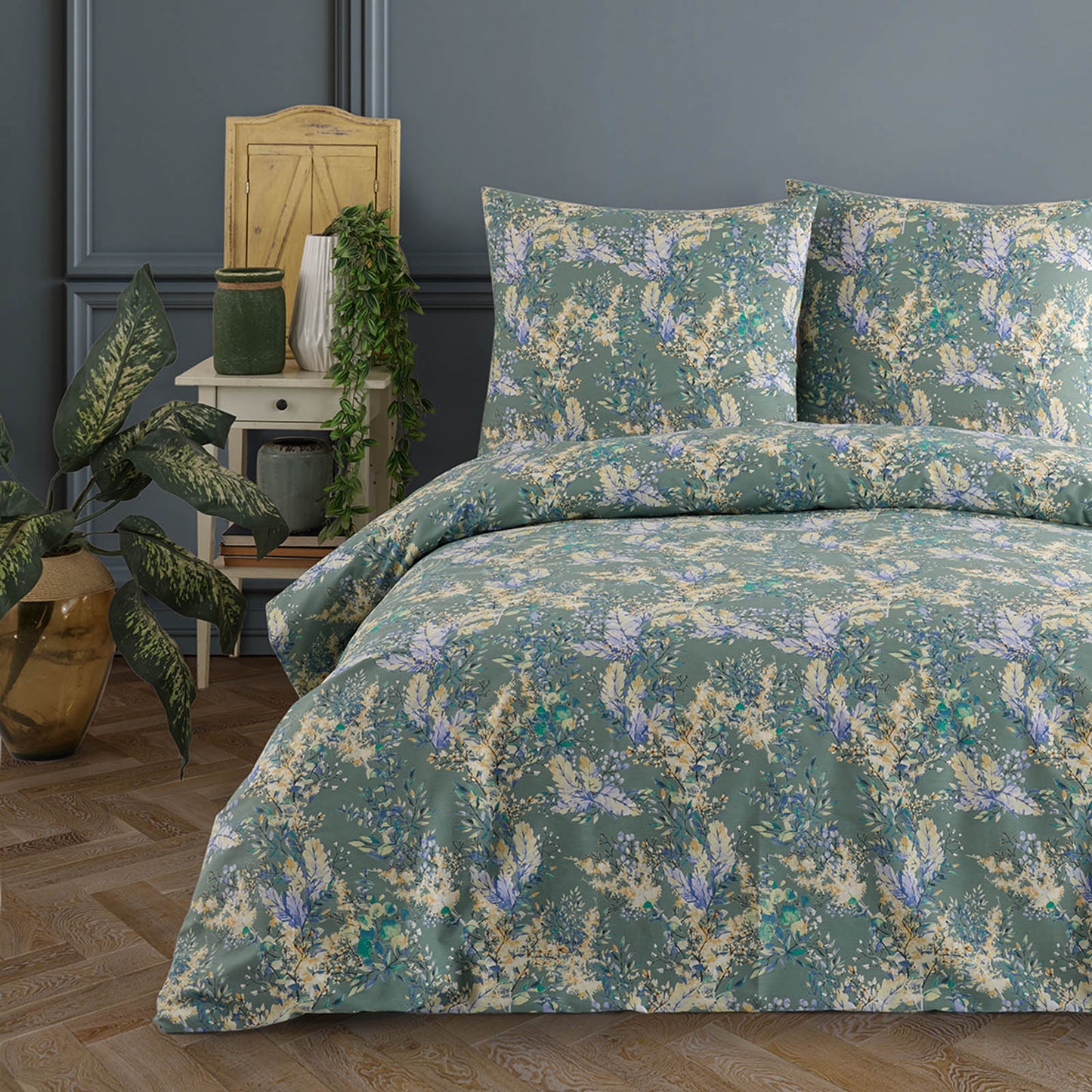 Doppelbett mit grün gemusterter Bettwäsche mit floralen Elementen in Blau, Gelb und Weiß, dekoriert in einem stilvollen Schlafzimmer mit Pflanzen und antikem Nachttisch.
